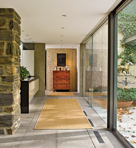 To unify the interior and exterior spaces, Dennis used masonry paving matrix for the floors of the terrace and throughout the house; the exterior and interior walls are all reinforced concrete. The blending of contemporary materials and period furnishings is seen at the end of the hallway where, placed against a concrete wall, a Connecticut tiger-maple chest of drawers, becomes a pedestal for a collection of pewter.