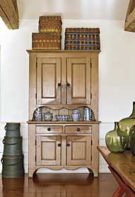 The New Jersey step-back cupboard with dramatic scalloping retains its original tan paint. “I think the wear pattern is as interesting as the paint,” says Patrick Bell. “It becomes a design element.” Woodlands baskets provide color on top of the cupboard, as does the graduated stack of firkins with original blue paint. Displayed on the cupboard is a portion of the wife’s extensive collection of blue-decorated spongeware. The nineteenth-century New England sawbuck table retains its original red paint and scrubbed top.