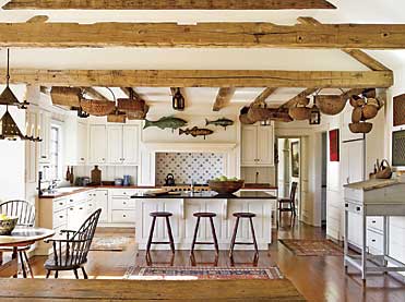 When home, the couple spends most of their time relaxing, cooking, and enjoying family in the kitchen. Patrick Bell and David Guilmet of Bell-Guilmet worked with the owners to personalize the space. Because of its open plan, they warmed the space by using reclaimed hand-hewn beams to bring the eye down from the high ceilings. Part of the wife’s collection of antique candle lanterns and oak and ash splint baskets also provide visual depth. The cod weathervane on the left was one of the couple’s early purchases from Olde Hope Antiques; they purchased the other fish weathervanes from the firm as well. On the center island is a large treenware bowl and wooden cutting boards. Visible along the right wall is some of their game board collection, acquired for their checkerboard patterns and simple graphics and colors. The early nineteenth-century stretcher-base schoolmaster’s desk retains its original grey paint. Visible in the dining room beyond is a Hudson Valley naïve landscape. In front of the window on the left is a large oval maple hutch table from New York state; its original red wash remains on the base. The Windsor chairs and stools are reproductions. The early nineteenth-century chandelier is from the Lammot du Pont Copeland collection.
