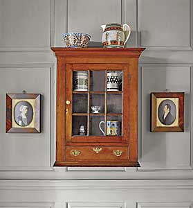 The Pennsylvania Chippendale cherrywood hanging wall cabinet, circa 1790, was purchased at Sotheby’s in 2002 from the Gunston Hall Plantation collection. Within and on top of the cabinet is part of the couple’s collection of mocha ware. One of a pair of portraits by “Mr. Boyd” flank the cabinet.