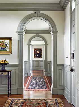 Holding a place of prominence at the end of the hall, the portrait of an unknown man from Union, Maine, circa 1840, by John Usher Parsons, was purchased from Joan Brownstein. Lining the floor is a rare pair of Sarouk Farahan rugs, circa 1890s. In the foreground is a Maine paint-decorated stand with faux-marble drawer front. A turned and painted tazza with collection of stone fruit is below a hand-painted theorem. The front door lock and handle are eighteenth century, in keeping with the owners’ intent to integrate period material into the house.